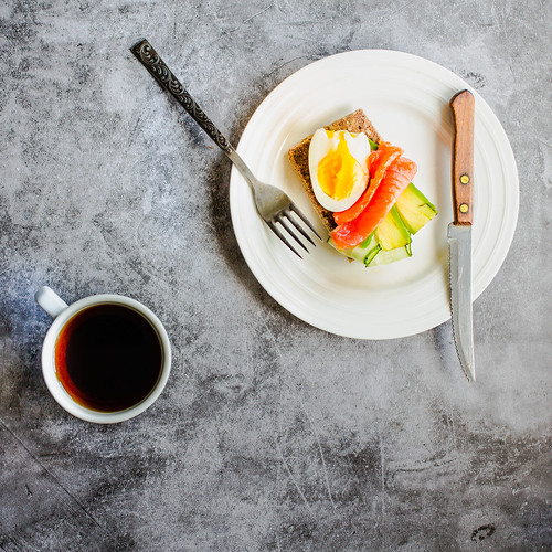 Gluten-free toast with avocado and fresh salted salmon, eggs and cuo of coffee on a gray background. Top view. Space for text. High protein and low carb meal. Insta-size