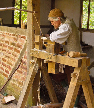 Tom the wood turner uses a pole lathe to fashion a wooden spoon in Little Woodham Living History Village