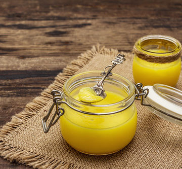 Pure or desi ghee (ghi), clarified melted butter. Healthy fats bulletproof diet concept or paleo style plan. Glass jar, silver spoon on vintage sackcloth. Wooden boards background