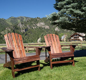 Two empty wood adirondack chairs sit on grass, overlooking the Sawtooth mountains of Idaho. Taken in Ketchum, ID